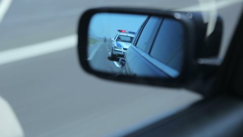 Yerevan, Armenia - June 2020 - Police car in the side mirror chasing a car on highway. Police chase, the car is running away from the chase
