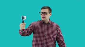 A young man in a plaid shirt takes pictures of himself, waves his hand at an action camera, conducts a video blog.