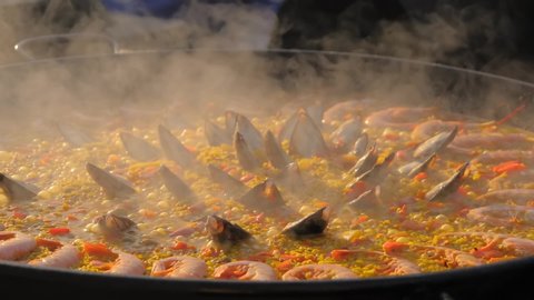 Slow motion: process of cooking paella with shrimp, mussel, rice, spice, saffron in huge paella pan at summer outdoor food market: close up. Spanish cuisine, seafood, gastronomy, street food concept