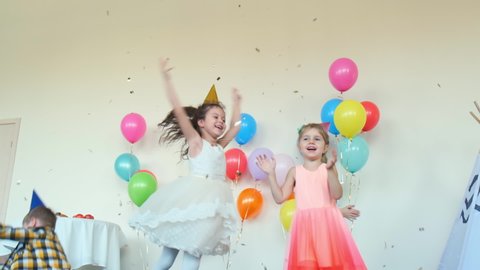 joyful little boys and girls dance in decorated room with wigwam and color balloons at funny birthday party slow motion
