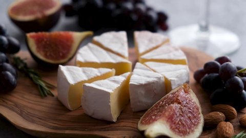Taking slice of camembert cheese. Cheese plate with figs, wine, grapes and almonds