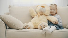 4k slowmotion video of little blond girl waving hello using teddy bear's paw.