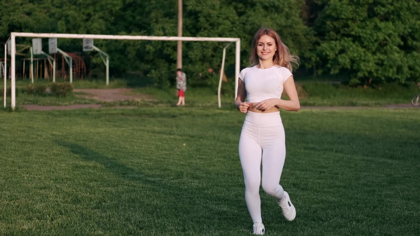 A eautiful woman is jogging on the grass. The sporty woman is wearing sportswear.She is living active life.