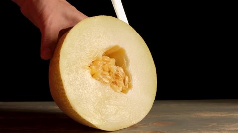 The girl cuts off a piece of melon with a large knife.