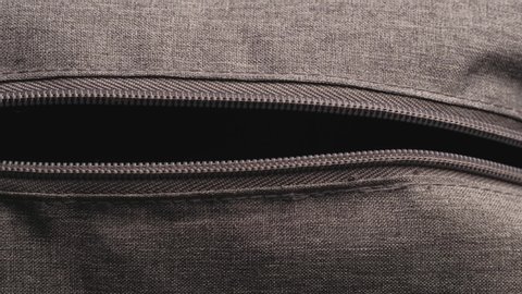 close and open zipper with metal slider body with leather pull tab of gray cloth bag by hand in low light mood.