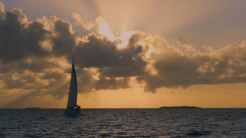 Sailboat against brilliant orange sunset near Isle of Pines, New Caledonia. Slow motion.