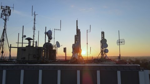 Silhouette of electromagnetic towers with satellite dish, microwaves and panel antennae at rooftop station during golden. Motion footage.