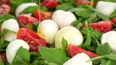 pour olive oil on Italian salad with mini mozzarella, tomatoes cherry and arugula rotating