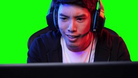 Asian gamer man playing game and looking at screen on PC computer at home. Asian man controlling console with mouse and keyboard. Young man leisure digital game with green screen.