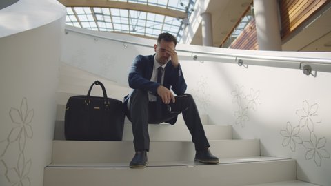 Dismissed businessman frustrated and desperate sitting on staircase in business center. Unhappy young entrepreneur sitting on stairs worry about financial crisis and unemployment