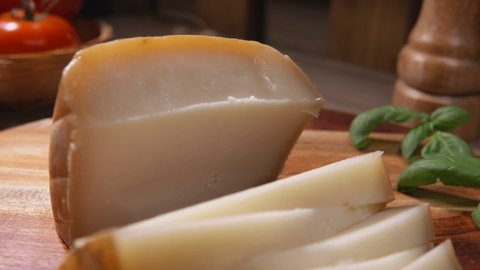 Close-up panorama of semi-hard sheep cheese cut in triangular pieces laying on the wooden board with basil