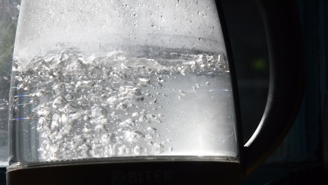 Blurry bubbles in hot water boiling inside glass teapot in bright sunlight. Close-up of boiling water in old transparent kettle on kitchen