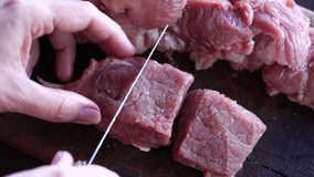 Closeup view 4k video footage of woman cutting pork meat at home using wooden board and knife to chop meat into small pieces