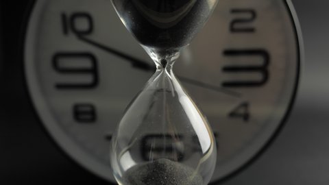 Extreme close up of a transparent hourglass with flowing black sand on blur dial background. Old classic timer. Time concept 4k