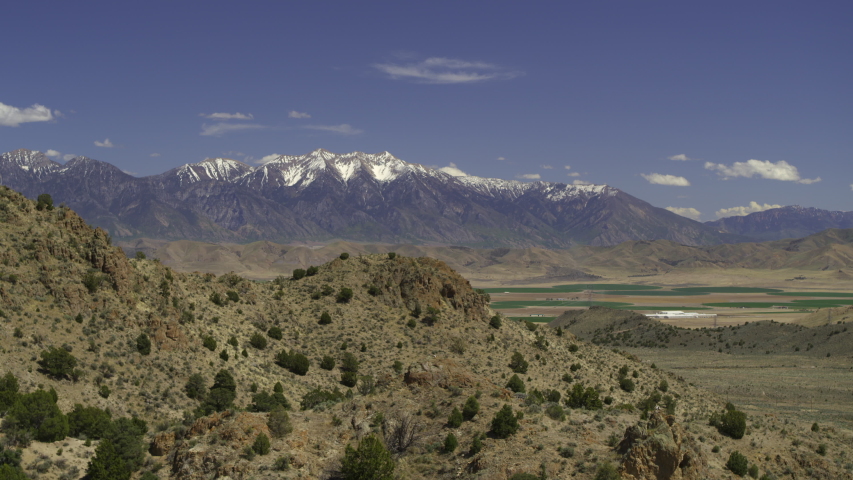 Aerial flyover passing hills near mountain range / Elberta, Utah, United States