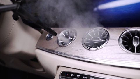 Zooming FHD shot of a hot steam cleaner cleaning the air conditioning vents in a futuristic car dashboard, with hot steam coming out of the vents. Hot steam cleaning of a car dashboard ventilation.
