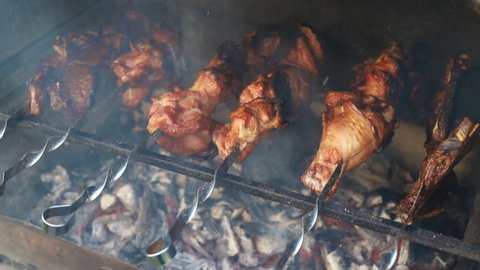 Closeup view of barbeque brazier cooking big turkey or chicken meat leg on metal skewers set flaming on burning coal with fire flame and smoke. traditional east european bbq party home backyard food