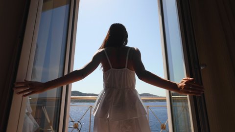 Authentic shot of an young woman is enjoying a panoramic view on a sea with yachts from a terrace of a hotel room during summer vacation.