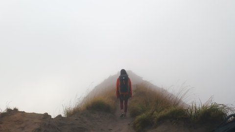 Aerial view of backpacker hiking in nature on top of foggy mountain. Woman tourist walking on mountain hill covered with thick mist. Travel and adventure concept