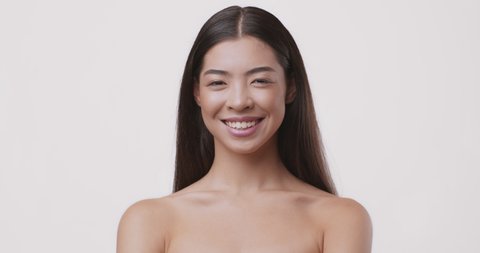 Portrait of attractive asian girl, opening eyes and smiling at camera, white studio background