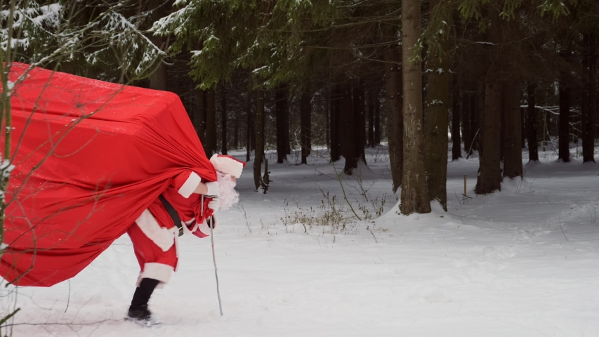 Santa with big bag of gifts is late for holiday, he looks at his watch and runs to congratulate people. concept of beginning of Christmas and New Year. Royalty-Free Stock Footage #1058033353