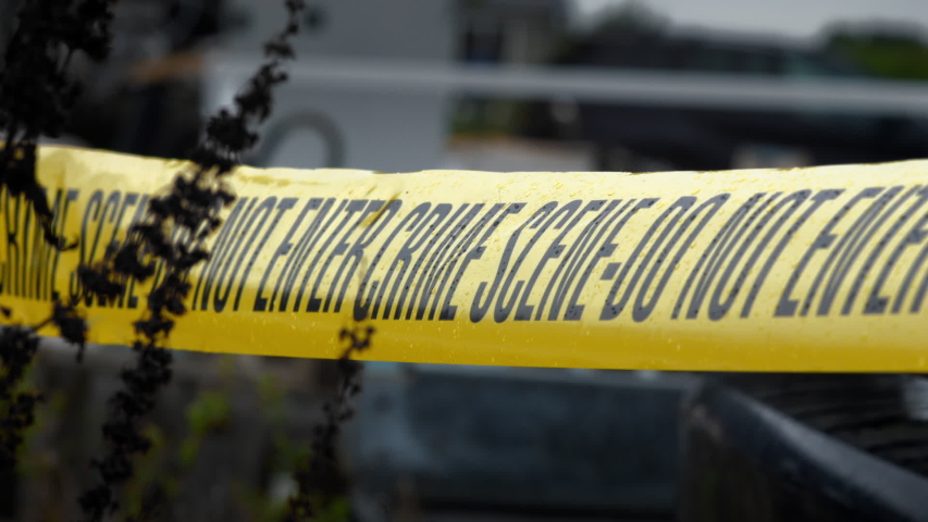 Police Crime Scene Cordon Tape Around Junkyard Ca. There is an overcast sky and light rainfall. Suggestive of the scene of a murder or hiding of a body. True-crime drama.
