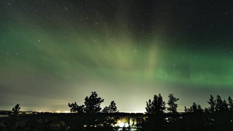 Winter Aurora Borealis green lights over city Umea and northern pine tree forest. Thin cold fog in air makes Northern Lights and stars mixed with city lights unclear and blurry. Sweden,Scandinavia