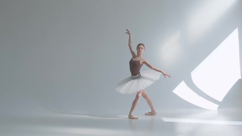 Young graceful ballerina in pointe shoes and white ballet tutu makes pirouette. Shot on a white background in the spacious and brightly lit studio. Slow motion.