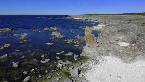 Aerial view of limestone rock formations, on the shore of Faro island, calm, sunny day, in Gotland, Sweden - static, drone shot