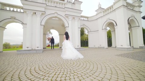 bride in a wedding dress runs to groom at sunset or sunrise against the backdrop of beautiful architecture. Slow motion. Europe. Fashion young woman goes to her husband hugs him and kisses Slow motion