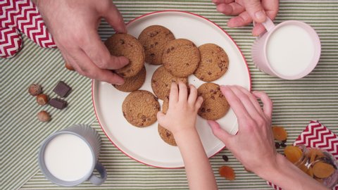 Top view hands take fresh cookies from plate. Woman's, men's and child hands take fresh home cookies. Many hands take one by one cookies. Cute family snack