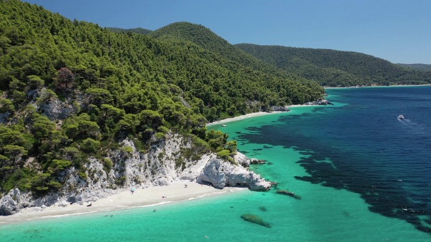Aerial drone video of tropical paradise island covered in pine trees with turquoise crystal clear beach in Mediterranean paradise destination