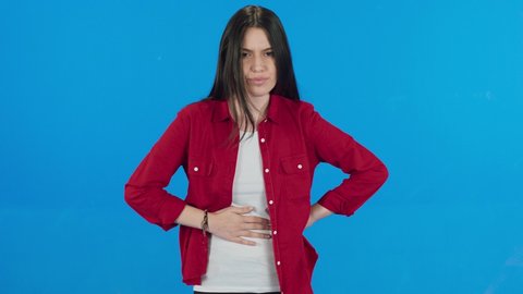 Female suffering from digestive problems. Bearded woman wearing white t-shirt sudden stomach ache, severe abdominal pain, constipation, gastritis, pancreatic diseases. Blue background.