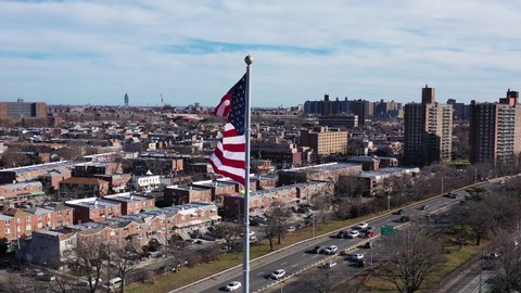 An aerial orbit,ing counter clockwise around the American flag which is blowing in the wind. Shot near the Belt Parkway in Brooklyn, New York on a sunny day, as traffices by smoothly below