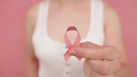 Pink october, breast cancer awareness ribbon in the hand of a young unrecognizable woman. High quality 4k footage
