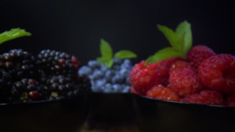 Bowls full of fresh forest fruits. Blackberries, blueberries, raspberries in black bowls, on a black background. Probe lens dolly unusual view