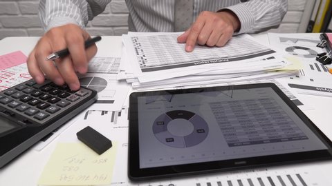 Business analysis and accounting concept - businessman working with document, spreadsheet, using calculator, tablet pc. Office desk closeup. 
