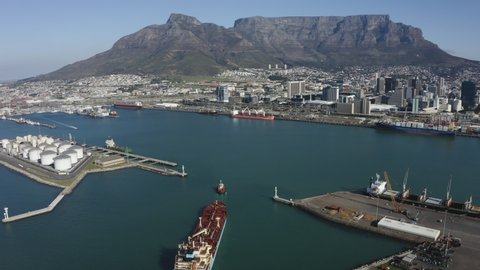 Epic landscape Table Mountain scenery. Aerial view of a tug boat towing a merchant ship into Cape Town Harbour South Africa

