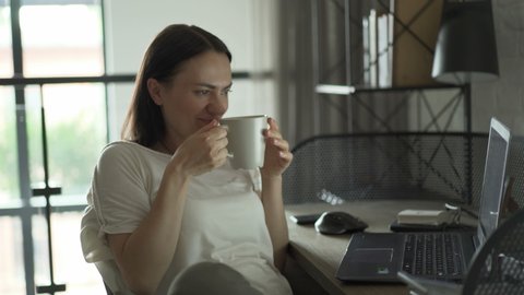 Beautiful woman drinking coffee and working on her laptop