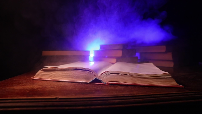 A stack of old books. Vintage book on wooden table. Magic lightning around a glowing book in the room of darkness. Selective focus | Shutterstock HD Video #1058061991