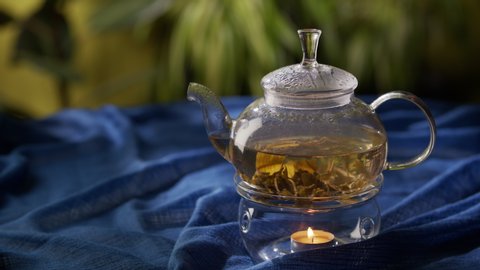 Tea party or tea ceremony. A woman stirs green tea in a glass teapot that is heated by a candle. The tea leaves swirling inside. A sense of comfort, warmth and home. Eco-friendly products, lifestyle
