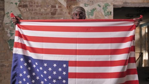 African american army man in camouflage bandana holding USA flag upside down protesting against racism. Bearded dark-skinned military male using US flag to transmit distress signal in this way