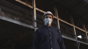 worker, foreman, builder, engineer, architect in dark shirt, white helmet, mask is at facility, at construction site, communicates via phone video communication, shows project, talks, reports on work