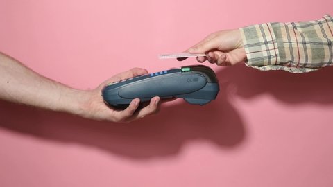 Woman pay by card. NFC payment terminal on a white table. Credit card or phone pay pos banking device, card machine in male hand on pink background