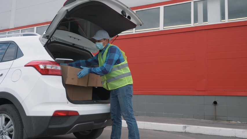 Volunteer wearing a mask and gloves delivers parcels. Online shopping during the covid-19 coronavirus pandemic. Contactless delivery of goods by courier service. Delivery during the coronavirus period Royalty-Free Stock Footage #1058072977