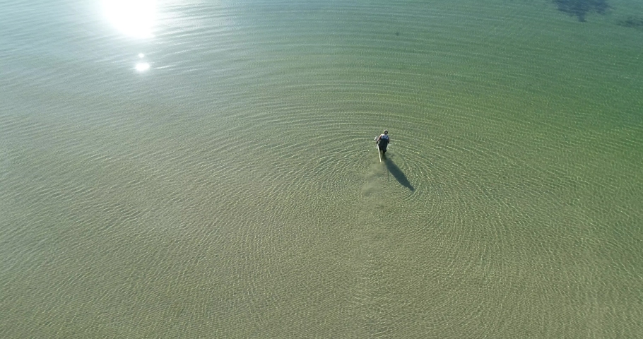Gold digger with metal detector on a sandy beach. Man with a metal detector and scoop searches for treasures. Clear water. Aerial view.