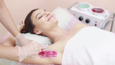 A master applies depilatory wax to the armpit of a young beautiful woman to remove unwanted hair. Sugaring. Depilation. Epilation. Beauty Concept. 
Selective focus on a girl's armpit with wax applied.
