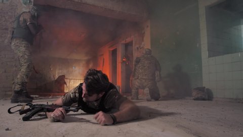 Injured military man crawling on his belly on durty floor of smoky ruined building trying to leave place of shelling. Strong-willed wounded army male saving his life during shootout