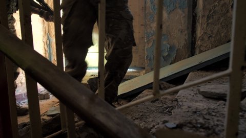 Close-up of army males feet in durty ankle boots walking up stairs in dusty ruined building during military anti-terrorist operation. Squad of soldiers storming enemy building, close-up of stair steps