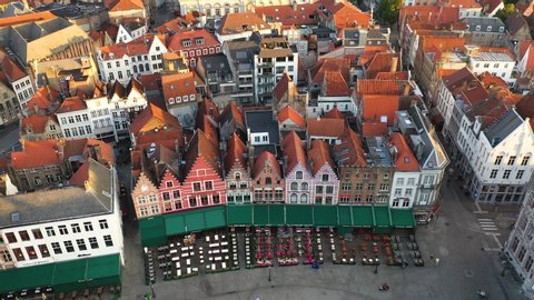 Aerial descending shot of pretty architecture in the market square of Bruges. Colorful historic restaurants and rooftops being lit by the morning sun.